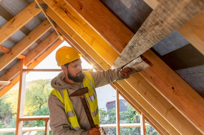 A man in a yellow helmet working on a roof beam