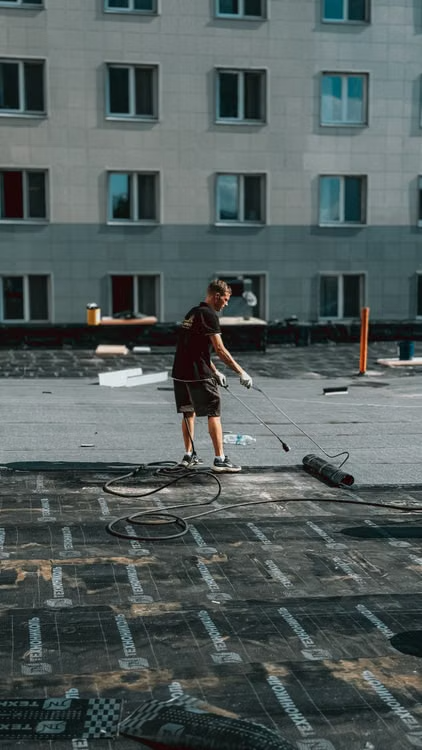 a construction worker applying roofing material on the top of a building